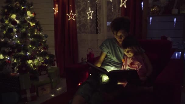 Mutter und Tochter lesen Buch über den Hintergrund des Weihnachtsbaums — Stockvideo