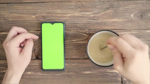 Tasse mit Tee und Smartphone mit Chroma-Schlüssel auf dem Tisch und männlichen Händen. Adobe-Ansicht — Stockvideo