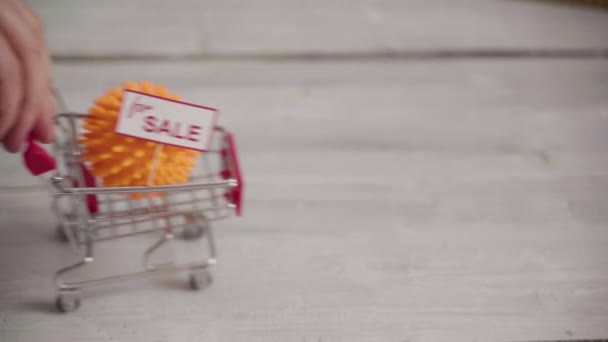 Masanın üzerinde Coronavirus şeklinde bir top olan küçük alışveriş arabası. — Stok video