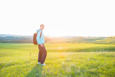 Sırt çantasıyla sahada yürüyüş yapan gülümseyen genç kadın.