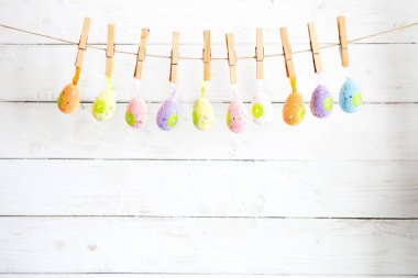 Beyaz ahşap arka planda ipin üzerinde asılı renkli paskalya yumurtaları.