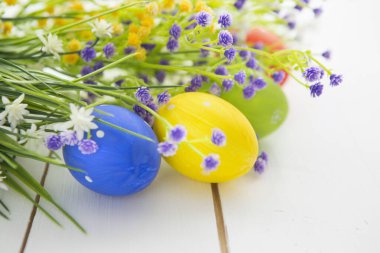 Beyaz ahşap bir yüzeyde güzel kır çiçekleri olan Paskalya yumurtaları. Paskalya geçmişi. Mutlu Paskalyalar.