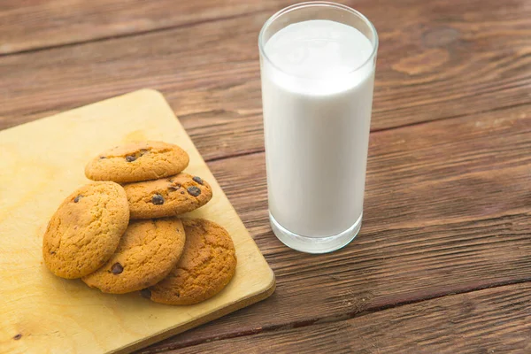 素朴な木製のテーブルの上にガラスの牛乳とチョコレートチップクッキー — ストック写真