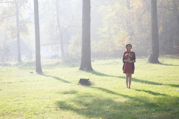 手に花を持つ森の妖精のイメージの少女 森の中を歩く女に太陽の光が当たる — ストック写真