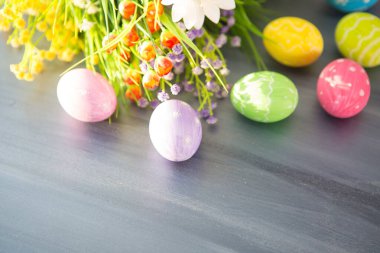 Renkli paskalya süslemesi ve gri ahşap bir masada çiçekler..