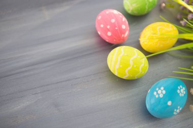 Paskalya yumurtaları süslemesi ve gri ahşap bir masada çiçekler..