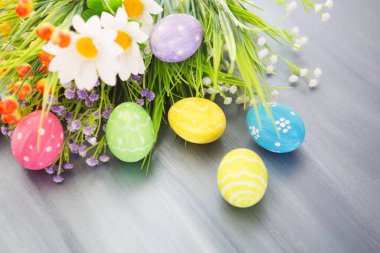 Boyanmış paskalya süsü ve gri ahşap bir masa üzerinde çiçekler..