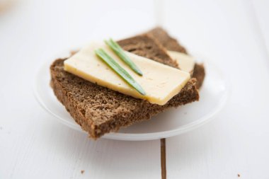 Peynirli siyah ekmek dilimi ve beyaz ahşap masada taze soğan.