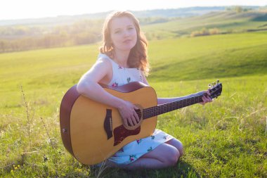 Gün batımında gitar çalan güzel genç bir kadın, moda tarzı.