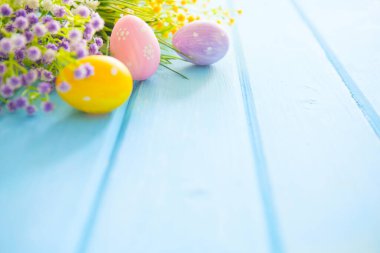 Mavi ahşap bir masada bahar çiçekleri ve renkli paskalya yumurtaları..