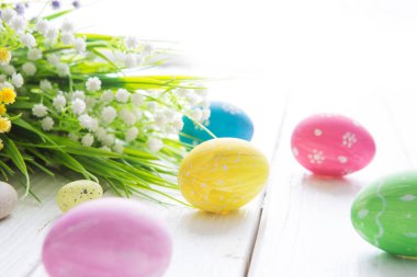 Renkli Paskalya yumurtaları ve bahar çiçekleri. Beyaz ahşap arka planda.