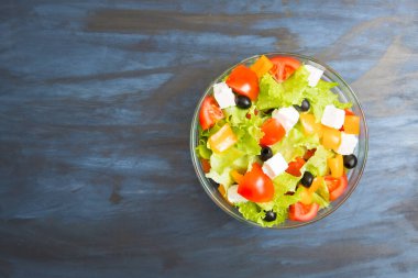 Siyah ya da koyu gri ahşap ya da metal masa üzerinde cam bir kasede Yunan salatası