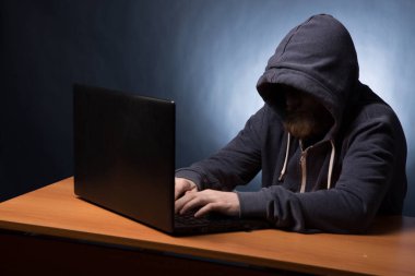 Kapüşonlu bilgisayar korsanı laptopla bilgi çalıyor.