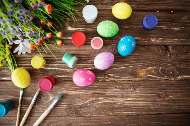 Renkli paskalya yumurtaları, palet boyası ve ahşap bir masada fırçalar. Kopyalama alanı olan üst görünüm