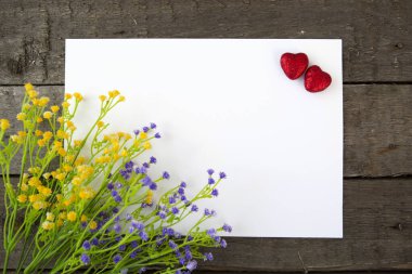 Çiçekler ve kalp şeklinde not kağıdı ahşap arka planda. Sevgililer Günü için aşk konsepti