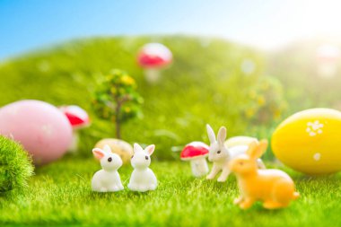 Mutlu Paskalyalar. Paskalya tavşanları yeşil çimlerin üzerinde paskalya yumurtası olan oyuncaklar. Plastik yeşil tarlada günbatımında plastik çimenler, mantarlar ve ağaçlar. Sahte ot. Makro.