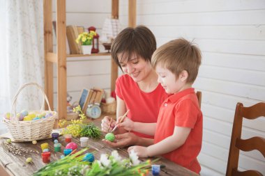 Anne ve oğlu renkli Paskalya yumurtaları boyuyorlar. Mutlu aile anne ve çocukları Paskalya yumurtalarını renklerle boyarlar. Paskalya tatili için hazırlık.