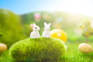 Mutlu Paskalyalar. Yeşil çimlerde renkli Paskalya yumurtaları ve tavşan oyuncakları. Plastik yeşil tarlada günbatımında plastik çimenler, mantarlar ve ağaçlar. Sahte ot. Makro.