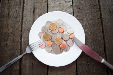 Tabaktaki bozuk paralar çatal ve bıçakla ahşap masada.