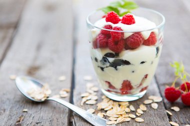Müsli, ahududu ve ahşap fonda siyah frenk üzümlü sağlıklı yoğurt tatlısı..