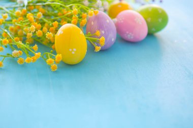 Mavi ahşap bir masa üzerinde Paskalya yumurtası ve çiçekler.