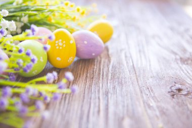 Kahverengi ahşap arka planda kır çiçekleri olan Paskalya yumurtaları.