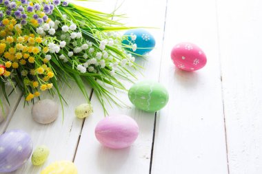 Ahşap masada renkli paskalya yumurtaları ve çiçekler.