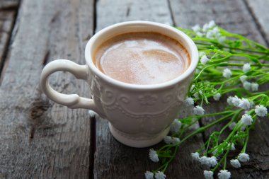 Masanın üzerinde bir fincan sade kahve ve beyaz çiçek. Kır çiçekleri