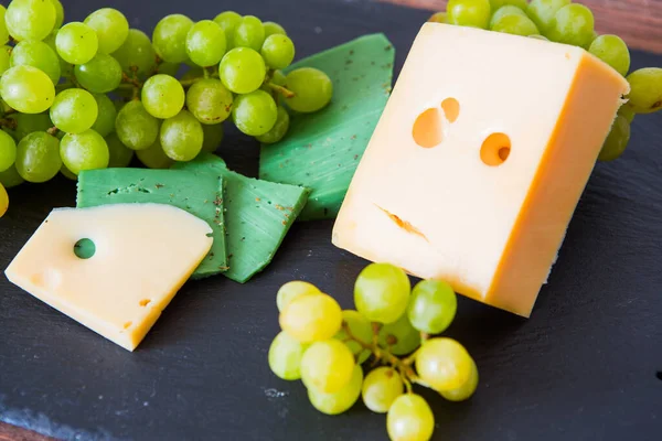 テーブルの上に黒スレートのチーズボード上の緑のブドウとチーズの様々なタイプ — ストック写真