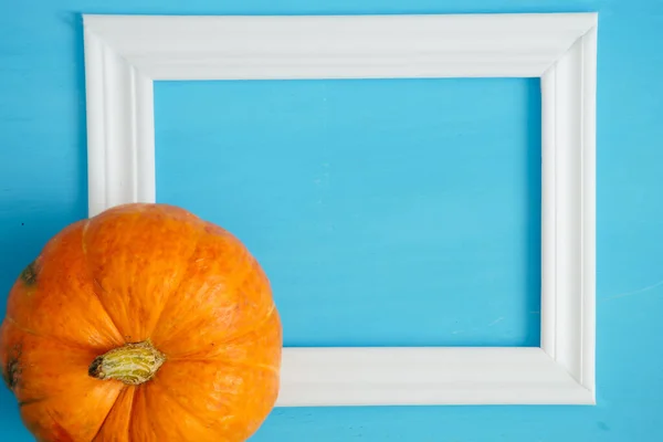 Pumpkins with white frame for picture on blue wooden background Thanksgiving and Halloween concept. View from above. Top view. Copy space for text and design