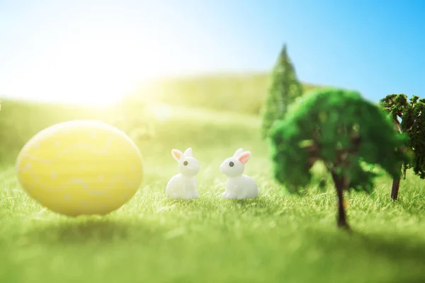 Happy Easter concept. Easter rabbits toy on a spring green grass. Fairy tale sunset on the plastic green field with plastic grass and trees.