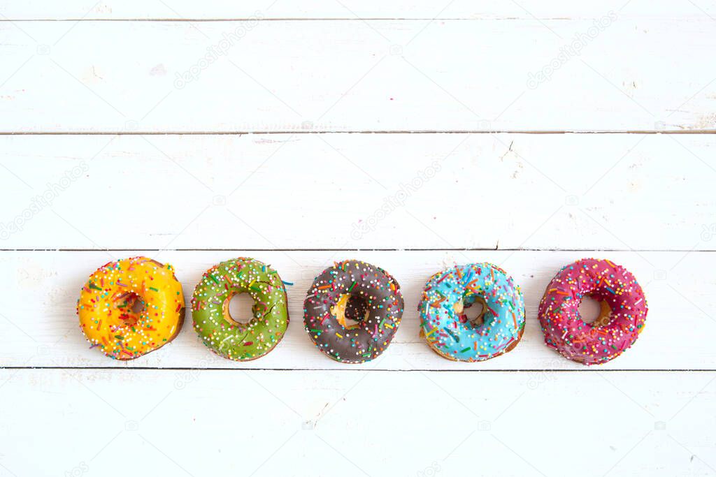 Sweet and colorful donuts on white wooden table with copy space. Top view.