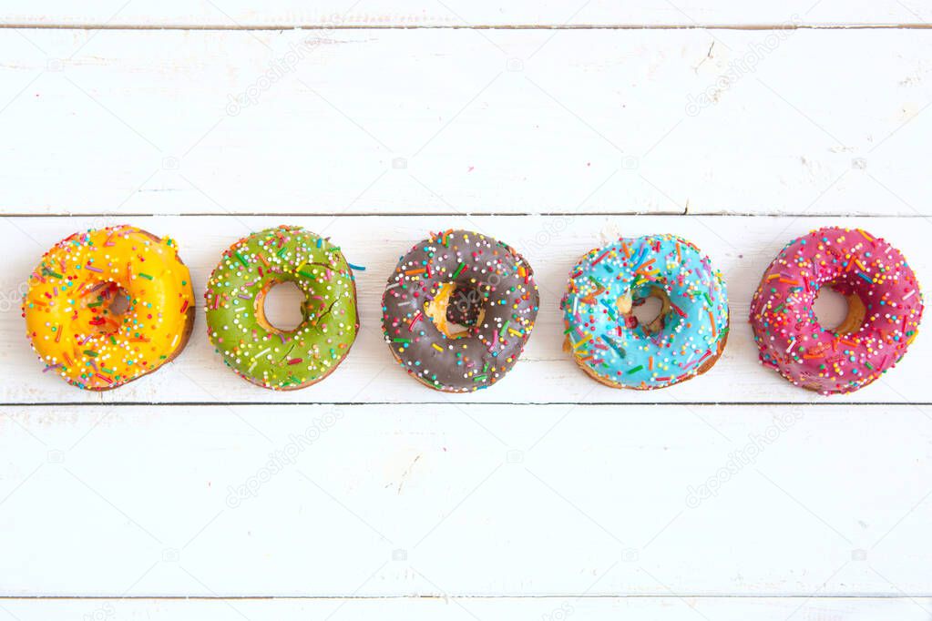 Sweet and colorful donuts on white wooden table with copy space. Top view.