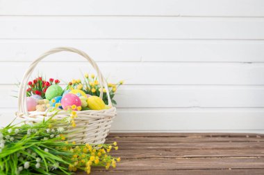 Sepette renkli paskalya yumurtaları ve tahta arka planda bahar çiçekleri. Tebrik kartı