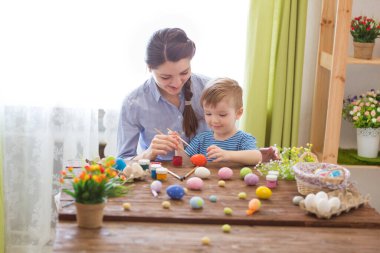 Paskalyayı kutlayan sevimli anne ve oğul. Paskalyayı kutlayan aile. Ebeveyn ve çocuk içeride oynuyorlar. Madalyalı ev ve bahar çiçekleri