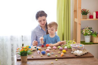 Paskalyayı kutlayan sevimli anne ve oğul. Paskalyayı kutlayan aile. Ebeveyn ve çocuk içeride oynuyorlar. Madalyalı ev ve bahar çiçekleri
