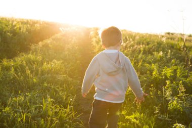 Sıcak bir yaz gününde, gün batımına karşı koşan bir çocuk.
