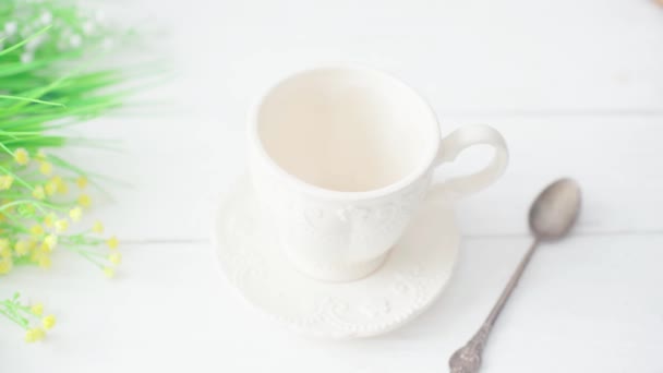 Köstlicher belebender Kaffee wird in eine schöne Porzellantasse auf einem weißen Tisch gegossen — Stockvideo