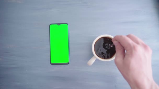 A mans hand uses a smartphone with a chroma key and mixes coffee with a spoon — Stock Video