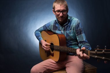 Koyu arkaplanda gitar çalan yakışıklı genç müzisyen.