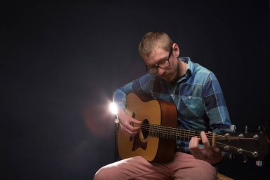 Koyu arkaplanda gitar çalan yakışıklı genç müzisyen.