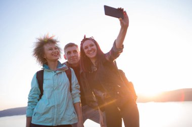 Bir grup arkadaş yürüyüş yaparken dağda dinleniyorlar. Yürüyüşçüler rahatlıyor ve selfie çekiyor. Dağlarda dağ yürüyüşünde selfie çeken arkadaşlar.