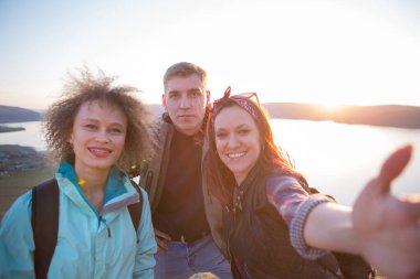 Bir grup arkadaş yürüyüş yaparken dağda dinleniyorlar. Yürüyüşçüler rahatlıyor ve selfie çekiyor. Dağlarda dağ yürüyüşünde selfie çeken arkadaşlar.