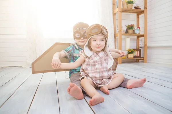 Happy children playing with vintage wooden airplane. Kids having fun at home. Imagination and freedom concept. Two little children wearing pilot costume and playing with old suitcase — Stock Photo, Image