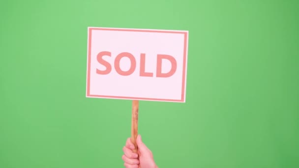 A mans hand raises a sign with the inscription Sold on a green background Chromakey — Stock Video