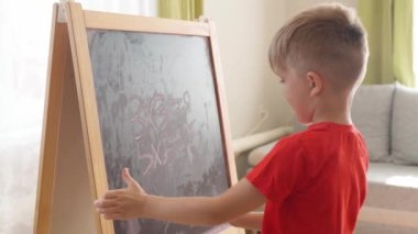 Küçük çocuk tahtaya matematik denklemleri yazar ve onları çözer.