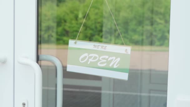 Un hombre cambia una señal que dice ABIERTO por una señal que dice CERRADO durante la pandemia de COVID-19. Placa de información en una puerta transparente o en una tienda. Movimiento lento — Vídeos de Stock