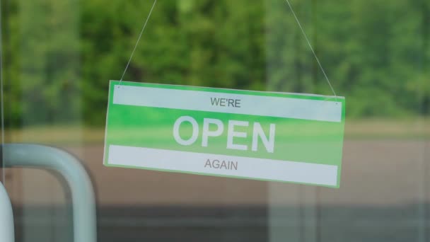 Un hombre cambia una señal que dice ABIERTO por una señal que dice CERRADO durante la pandemia de COVID-19. Placa de información en una puerta transparente o en una tienda — Vídeo de stock