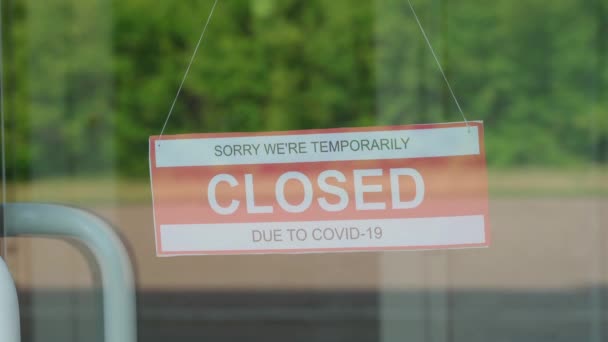 Ένας άνθρωπος αφαιρεί μια πινακίδα που έγραφε ΚΛΕΙΣΙΜΟ κατά τη διάρκεια της πανδημίας COVID-19 που κρεμόταν σε μια διαφανή πόρτα ή σε μια βιτρίνα — Αρχείο Βίντεο