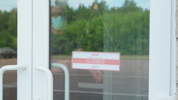 El hombre cambia el signo CERRADO por el signo ABIERTO. Placa de información en una puerta transparente o en una tienda durante la pandemia de COVID-19 — Vídeos de Stock